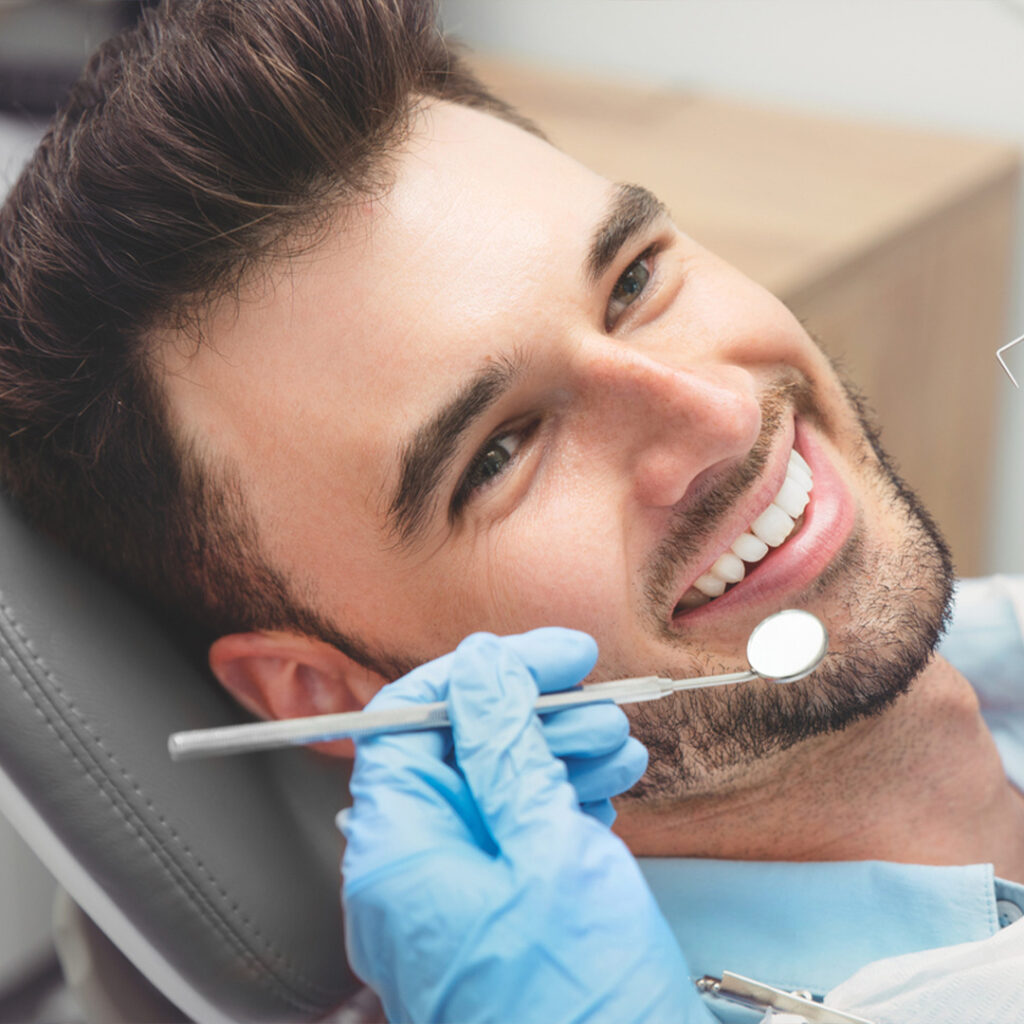 a male patient laying on a dental chair and a hand wearing a blue gloves while holding a mouth mirror