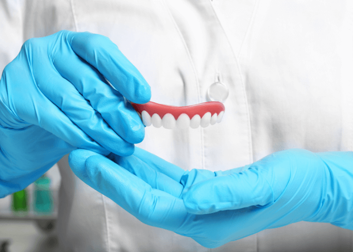 two hands wearing blue gloves holding a denture